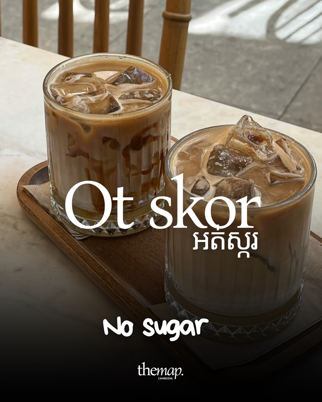 Two glasses of iced coffee on a wooden tray on a marble table, paired with the Khmer phrase for no sugar