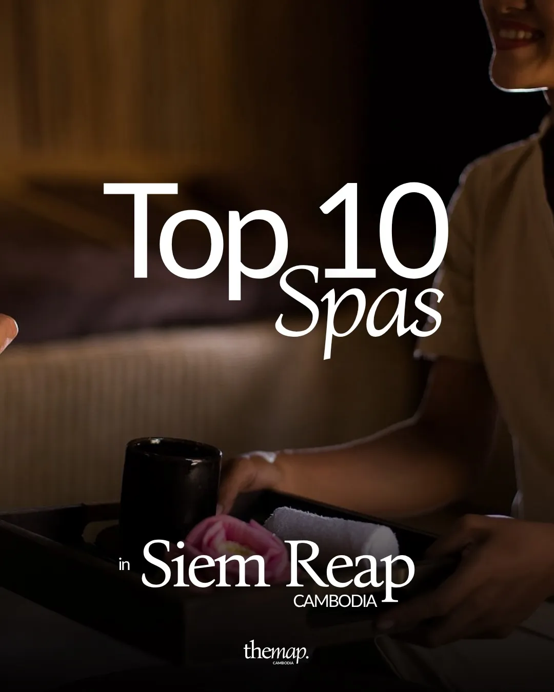 Spa therapist in Siem Reap carrying a tray with a lotus flower and rolled towel in a dimly lit treatment room